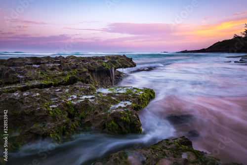 Tranquil Long Exposure of Smooth Ocean Water Coming over Rocks on Sandy Beach with Colorful Pastel Sunrise Sky at Dawn on Maui Hawaii in Relaxing Tropical Island Paradise 