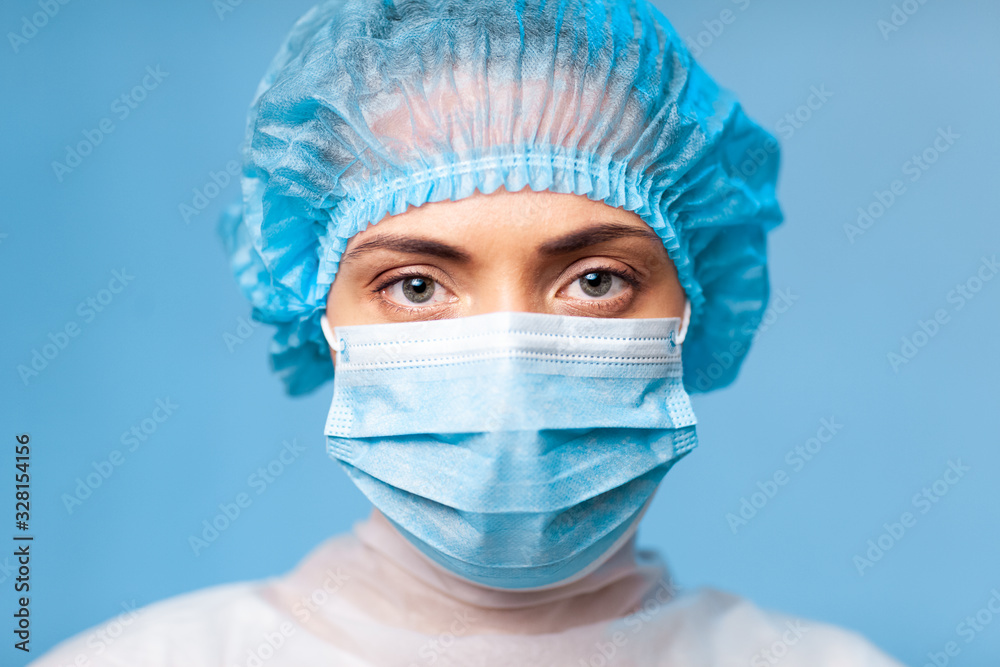 Portrait of a doctor, a young woman in a protective medical mask on her face and a cap on her head. looking seriously into the frame. on a blue background. surgeon. ambulance paramedic. copy space