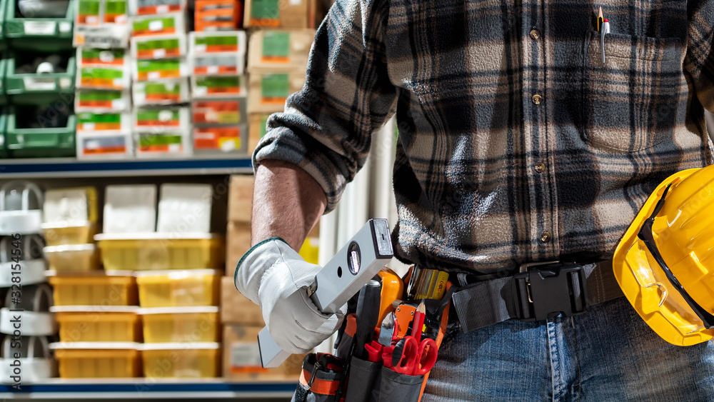 Electrician in the electrical parts store holds the level in hand, helmet with protective goggles. Construction industry, electrical system. Electrician in the electrical parts store holds the level in hand, helmet with protective goggles. Construction industry, electrical system.
