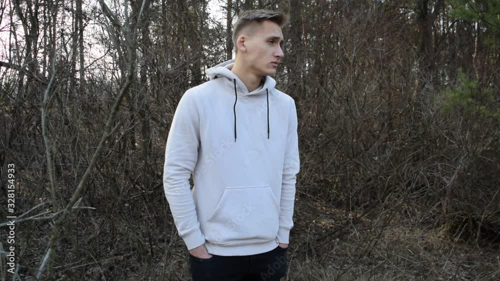 A young man in a white jacket stands against the gray nature of dry branches A young man in a white jacket stands against the gray nature of dry branches