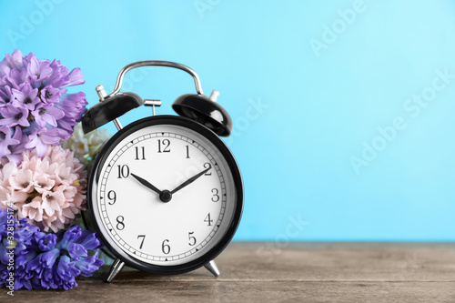 Black alarm clock and spring flowers on light blue background, space for text. Time change