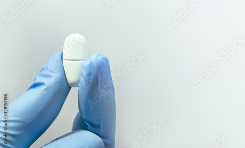 White capsule in hand in medical gloves