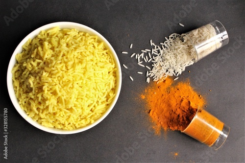 Bowl of yellow rice cooked from basmati rice with turmeric powder glass of rice,turmeric power beside the bowl. photo isolate on black top view
