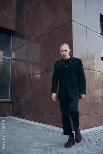 a bald guy in a black suit stands against the wall
