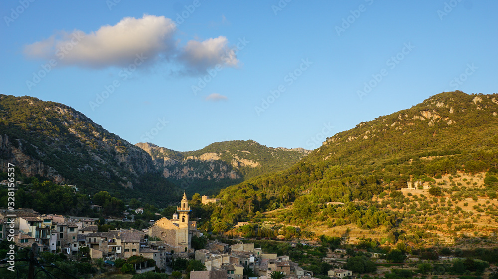 Picturesque Spanish village of Valldemossa in a valley surrounded by green mountains on the sunset 