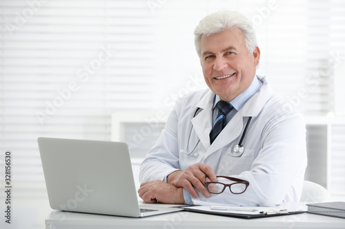 Portrait of senior doctor in white coat at workplace
