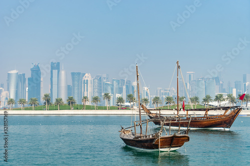 Retro historical boat with blurred panoramic view of modern skyline of Doha and green palms on background © Hladchenko Viktor