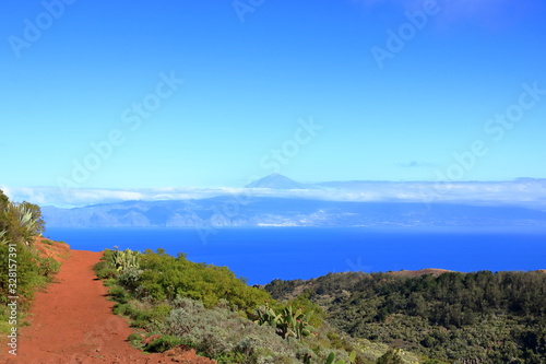 Colorful red earth and sand hills of volcanic origin above "Mirador de Abrante" in Agulo on La Gomera - looking north onto the atlantic ocean with Teide volcano on Tenerife