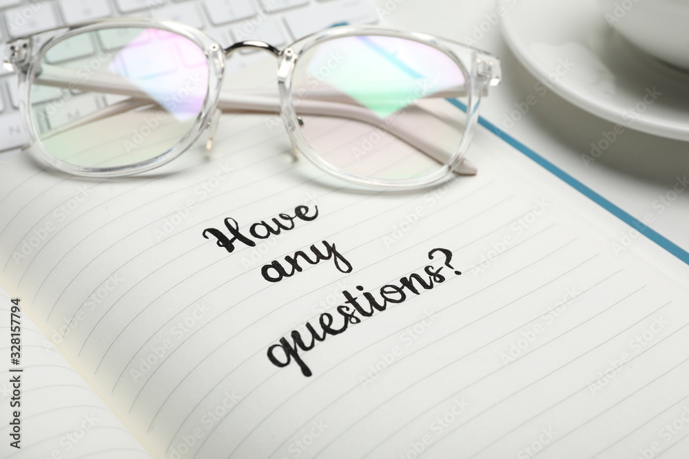 Notebook with phrase HAVE ANY QUESTIONS and eyeglasses on table, closeup Notebook with phrase HAVE ANY QUESTIONS and eyeglasses on table, closeup