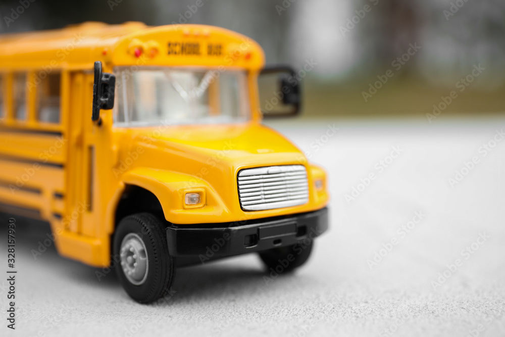 Yellow toy school bus against blurred background, closeup. Transport for students