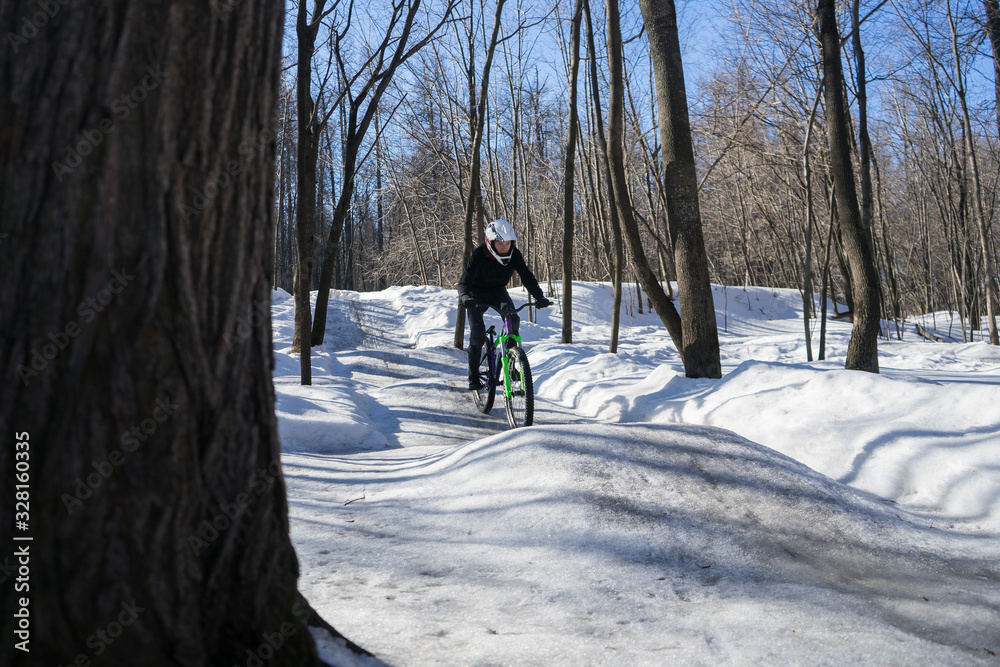 A cyclist in a helmet rides on a pump track in winter. Mountainbike rider rides a bike on a snowy track