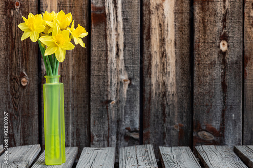 Fototapeta Naklejka Na Ścianę i Meble -  Bunch of bright yellow spring daffodils in a yellow glass vase on a rustic plank table.