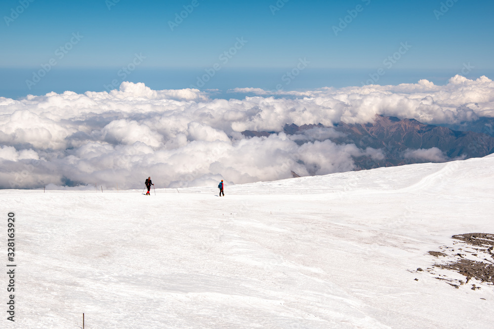 Landscape view of snow-capped hillside Mount Elbrus, Caucasus, Russia. A path leading down from the top. Two alpinists descending from the top. Clouds in the background.