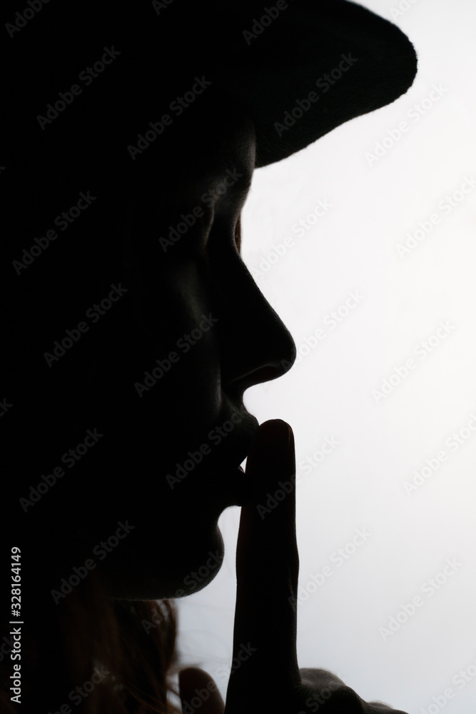 Silhouette portrait of young female model showing silence gesture. Black and white noir style