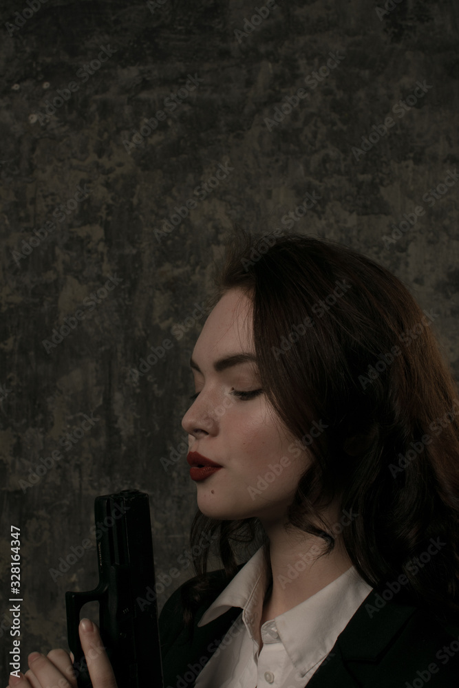 Obraz premium Vertical portrait of young brunette female model blowing on gun barrel. Female agent concept.