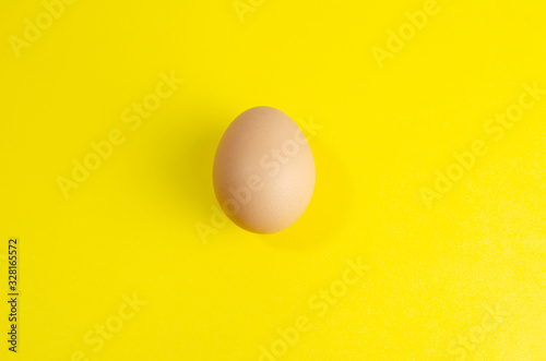 one fresh brown chicken egg on a yellow background