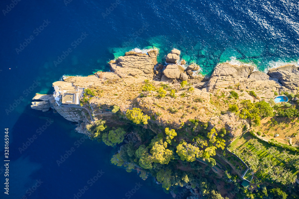 Top view on a lighthouse standing on the rocky hill near the sea with blue turquoise water in Portofino, Italy. Ligurian sea washes a coast with the big stones.