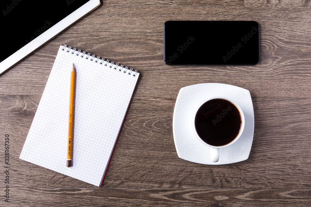 Smartphone and tablet PC with black screens on a wooden background with cup of black coffee. An opened notebook with pencil on it lie next to them. Smartphone and tablet PC with black screens on a wooden background with cup of black coffee. An opened notebook with pencil on it lie next to them.
