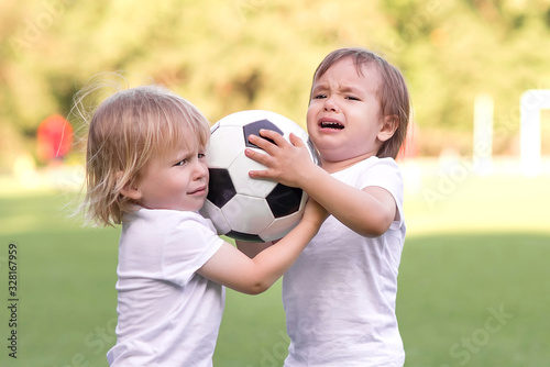 Fotografie Two little toddlers arguing at football field or playground over soccer ball trying to take or grab ball
