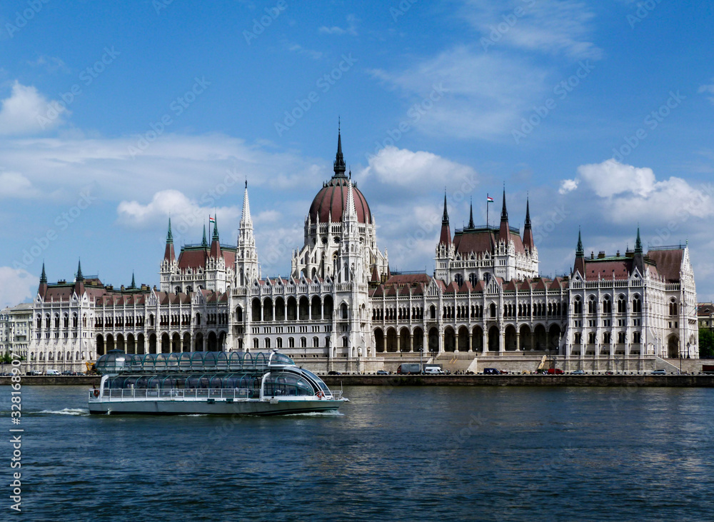 Fototapeta premium the Hungarian Parliament in Neo-Gothic style seen from across the Danube. Famous and popular landmark and tourist attraction in Budapest. panoramic view. white tour boat. City skyline. blue sky.