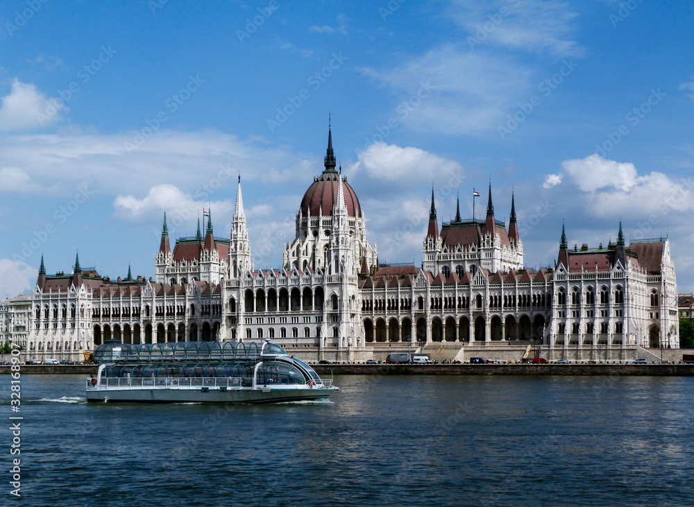 the Hungarian Parliament in Neo-Gothic style seen from across the Danube. Famous and popular landmark and tourist attraction in Budapest. panoramic view. white tour boat. City skyline. blue sky.