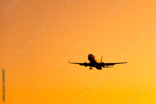 Large airliner passengers view is landing on the landing strip at the airport against the backdrop of bright orange sunset on a sunny summer day. A plane flies in the sky at sunset day © marina_larina