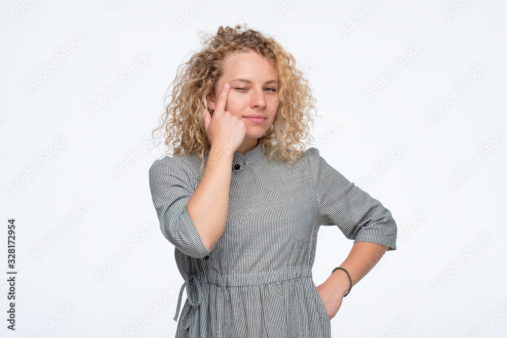 Curly woman is touching her eye to show that she has problem with eyesight.