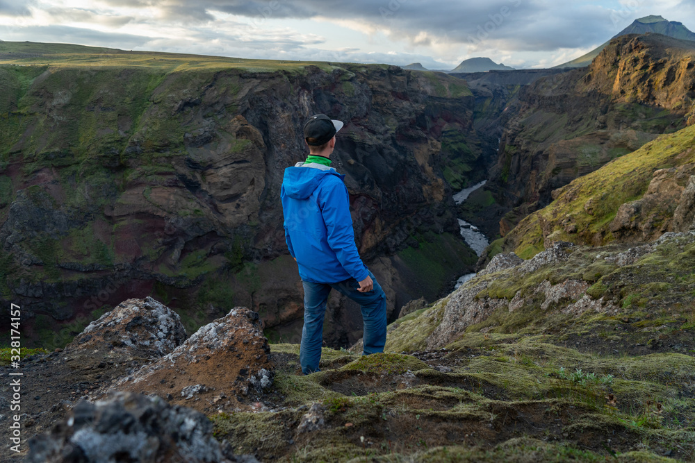 Caucasian young guy standing in over mountain and canyon background on the way of Laugavegur trail, Iceland. Promoting healthy lifestyle
