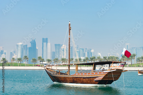 Retro historical boat with blurred panoramic view of modern skyline of Doha and green palms on background