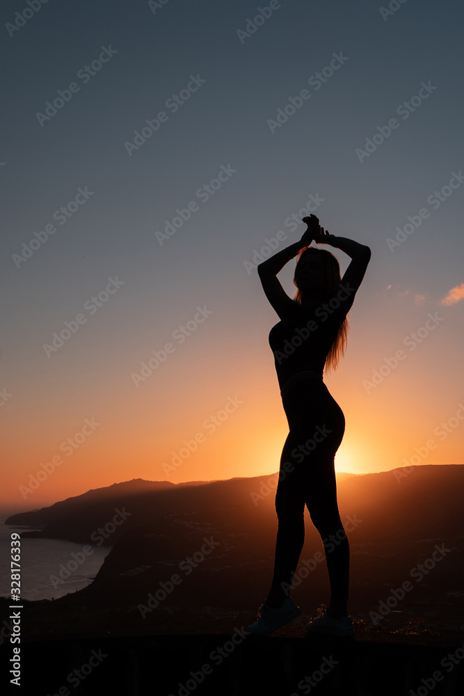 Silhouette of woman enjoying freedom feeling happy at sunset with mountains and sea on background