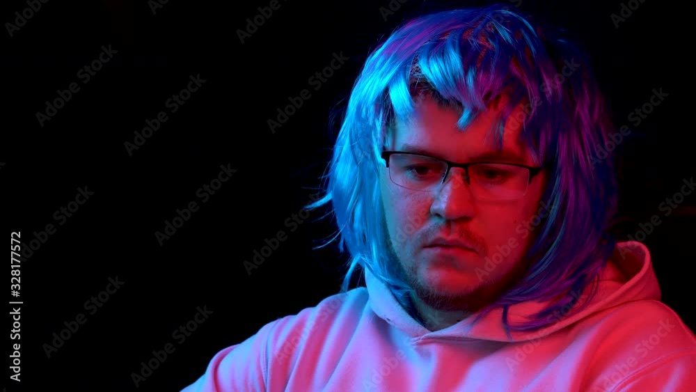 A young man sits at a computer in a blue wig. A man in a wig looks at a computer monitor. The camera moves because of the monitor. A young man sits at a computer in a blue wig. A man in a wig looks at a computer monitor. The camera moves because of the monitor.