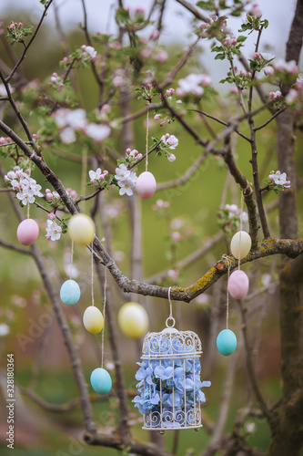 Beautiful decorative birdcage in the branches of a blossoming apple tree. Decorative easter eggs hanging on threads. Vertical frame
