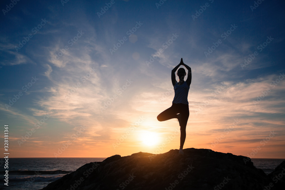 Silhouette of fitness yoga woman doing exercises on the sea beach during amazing sunset.