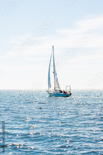 White sloop rigged yacht sailing in a Mediterranean sea on a clear sunny day, Spain. Blue sky with white clouds, reflections on water; photo