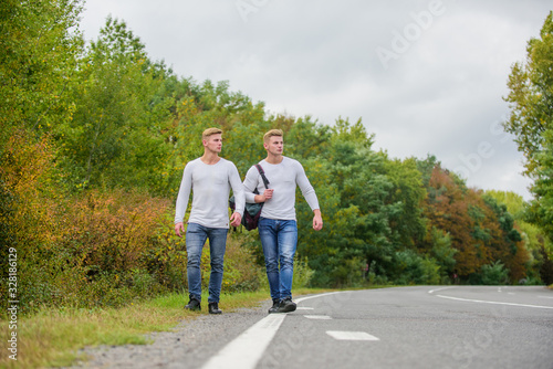 Guys hitchhiking on road. Tourist traveler travel auto stop. Transporting issues. Men backpack walking road. Twins walk along road. Brothers friends nature background. Long way. Adventure concept