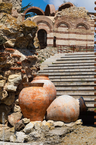 Ancient amphora in old town of Nesebar, Bulgaria. Ancient pottery pots. Three amphora against Church of St John Aliturgetos and Ancient Theatre