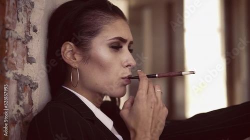 close up portrait adult smoking woman holding cigarette holder brunette with long hair in jacket and white shirt sitting in abandoned building