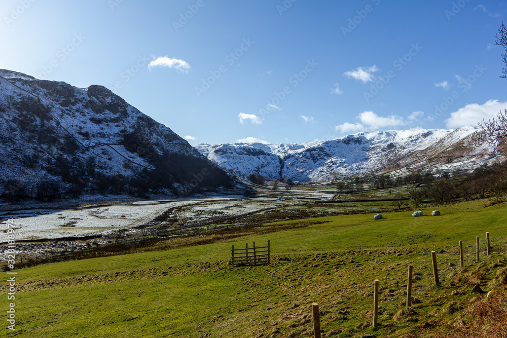 A scenic rural view of a snowy green field with mountain range slope in the background under a majestic blue sky