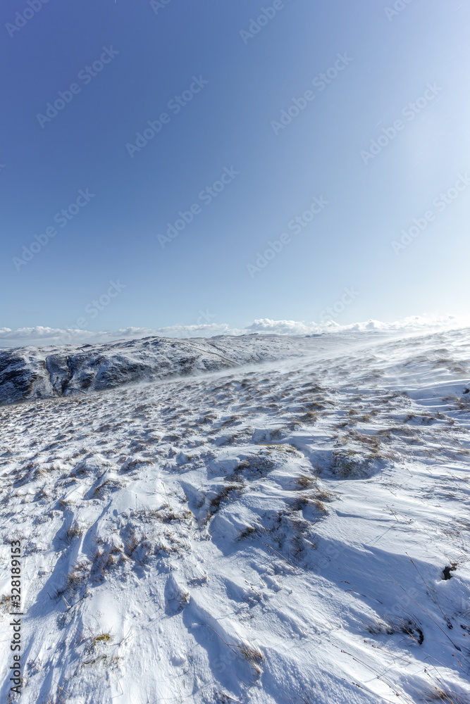 A scenic view of snowy slope with mountain range summit and some pine trees in the backgrounf under a majestic blue sky and some white clouds A scenic view of snowy slope with mountain range summit and some pine trees in the backgrounf under a majestic blue sky and some white clouds