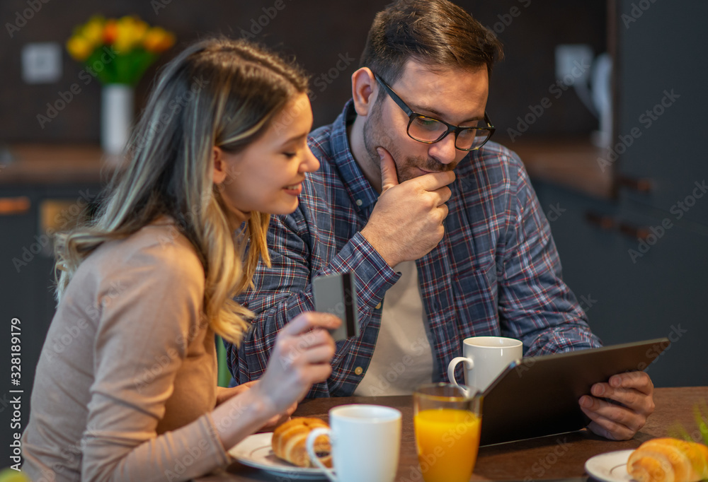 Happy couple using tablet and having breakfast in the kitchen Happy couple using tablet and having breakfast in the kitchen