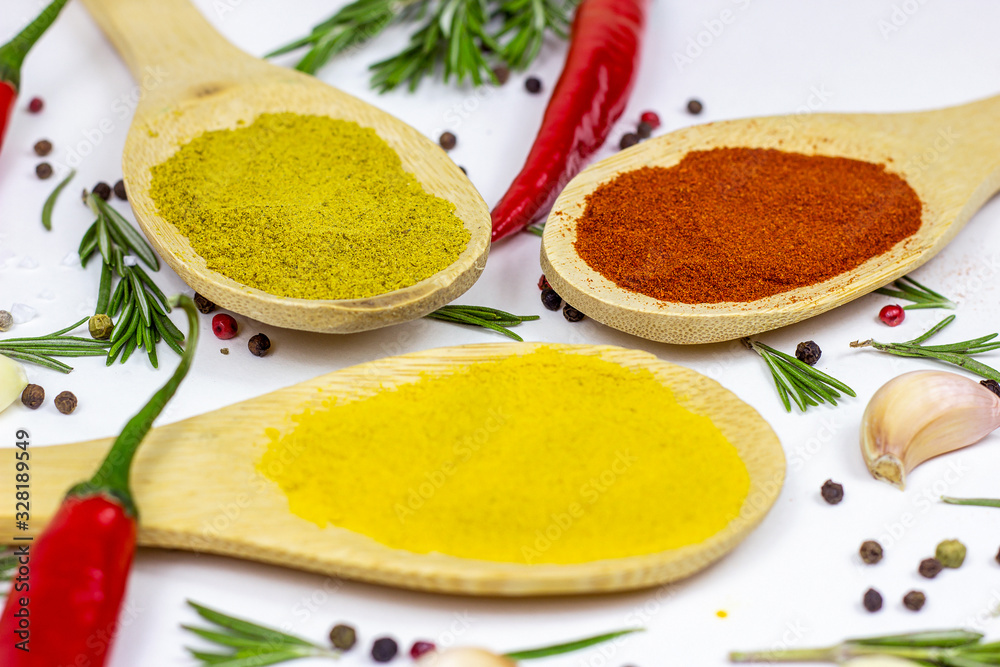 Variety of spices and seasonings (indian curry, different pepper, paprika powder, salt, dry ginger and curcuma) for cooking in wooden spoons on white kitchen table background Variety of spices and seasonings (indian curry, different pepper, paprika powder, salt, dry ginger and curcuma) for cooking in wooden spoons on white kitchen table background