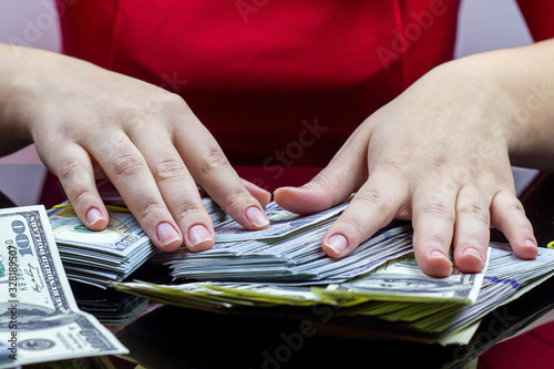 Woman in red dress holding and counting cash money (american dollars) in her hands on black table background. Profit and reward, bribe and graft, wealth and lottery win concept