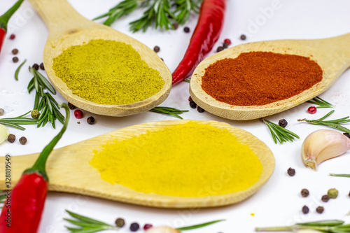Variety of spices and seasonings (indian curry, different pepper, paprika powder, salt, dry ginger and curcuma) for cooking in wooden spoons on white kitchen table background