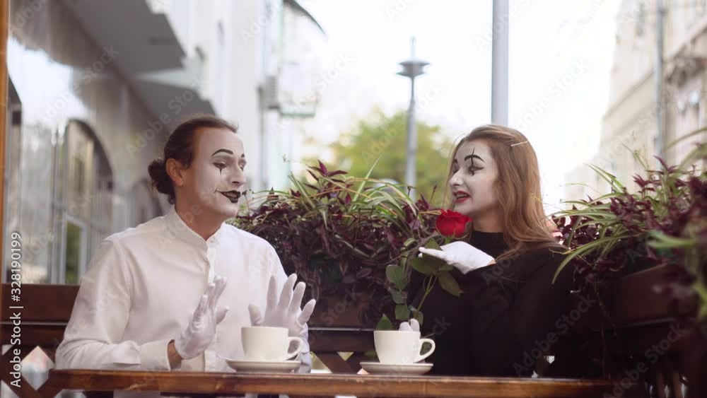 Two happy mime on a date in cafe. Happy man giving a flower to his girlfriend. Romantic date Two happy mime on a date in cafe. Happy man giving a flower to his girlfriend. Romantic date