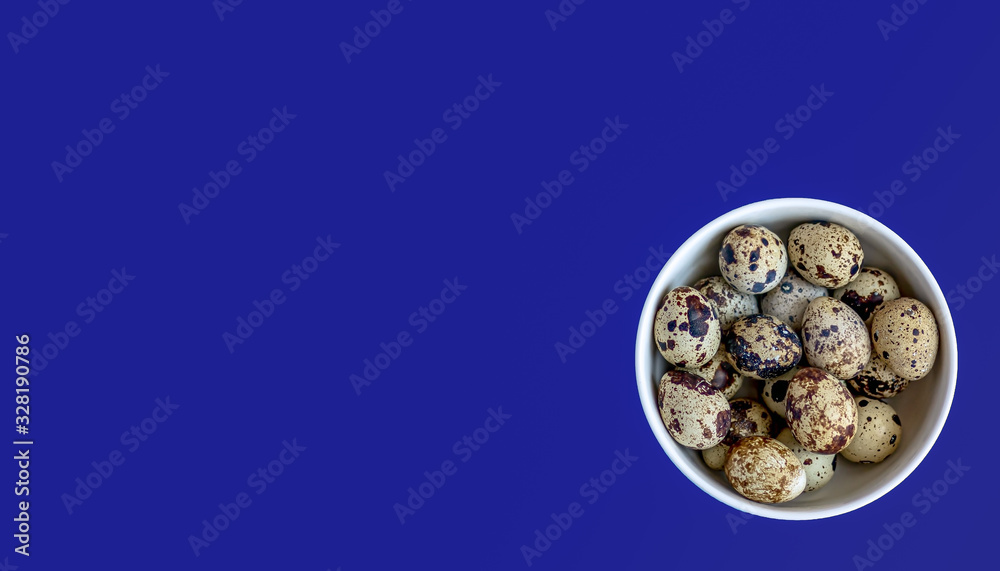 Quail eggs in a white bowl on a blue background. Top view. Copy space. Quail eggs in a white bowl on a blue background. Top view. Copy space.