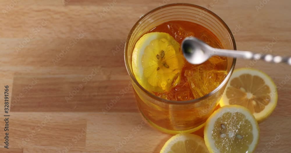 Hand placing sliced lemon into a rocks glass filled with iced cocktail then stirring beverage with bar stir spoon swirling ice and drink Hand placing sliced lemon into a rocks glass filled with iced cocktail then stirring beverage with bar stir spoon swirling ice and drink