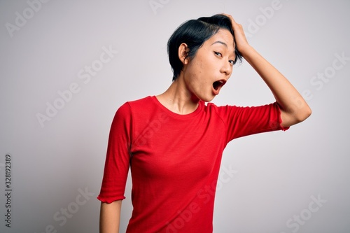 Young beautiful asian girl wearing casual red t-shirt standing over isolated white background surprised with hand on head for mistake, remember error. Forgot, bad memory concept. © Krakenimages.com