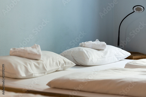 Fototapeta Naklejka Na Ścianę i Meble -  Cozy double bed with white sheets, and welcome towels on pillows, in comfortable online marketplace vacation apartment interior. Short-term, apartment rental bedroom interior