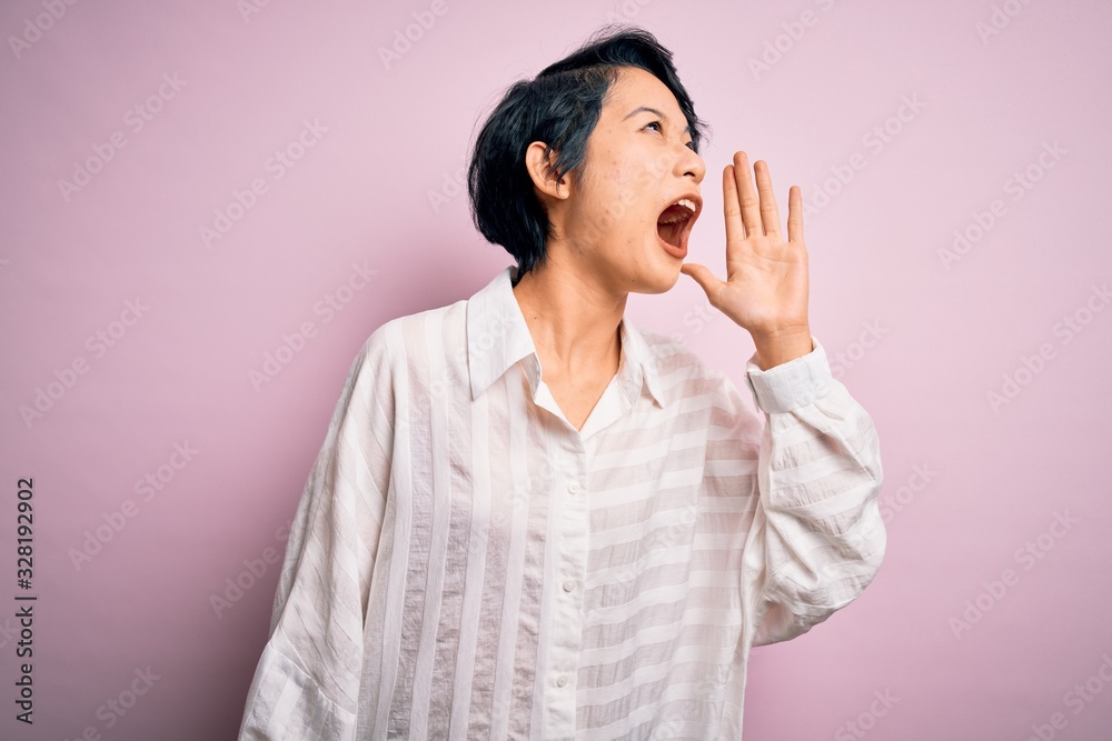 Young beautiful asian girl wearing casual shirt standing over isolated pink background shouting and screaming loud to side with hand on mouth. Communication concept. Young beautiful asian girl wearing casual shirt standing over isolated pink background shouting and screaming loud to side with hand on mouth. Communication concept.