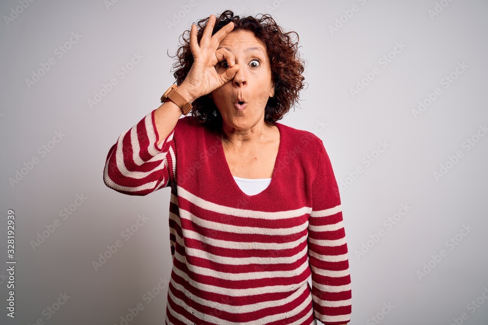 Middle age beautiful curly hair woman wearing casual striped sweater over white background doing ok gesture shocked with surprised face, eye looking through fingers. Unbelieving expression. Middle age beautiful curly hair woman wearing casual striped sweater over white background doing ok gesture shocked with surprised face, eye looking through fingers. Unbelieving expression.